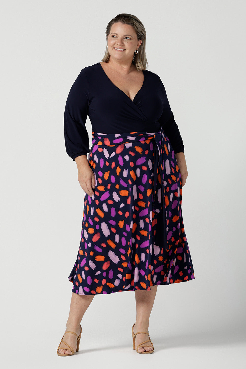 Size 18 curvy woman wears the Nerida dress. Functioning fit and flare wrap dress with a navy bodice and printed skirt. 3/4 Sleeves and functioning pockets. Made in Australia for women. Size 8 - 24. Styled back with a brown sling back heel. 
