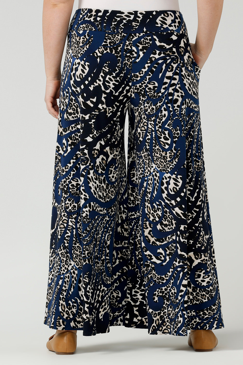 Back view of A curvy size, size 12 woman wears printed wide leg pants with pockets with a navy round neck top. These pull-on, easy care pants are comfortable for your everyday workwear capsule wardrobe. Shop these Australian-made wide leg trousers online in sizes 8 to 24, petite to plus sizes.