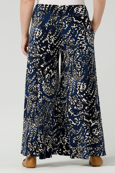Back view of A curvy size, size 12 woman wears printed wide leg pants with pockets with a navy round neck top. These pull-on, easy care pants are comfortable for your everyday workwear capsule wardrobe. Shop these Australian-made wide leg trousers online in sizes 8 to 24, petite to plus sizes.
