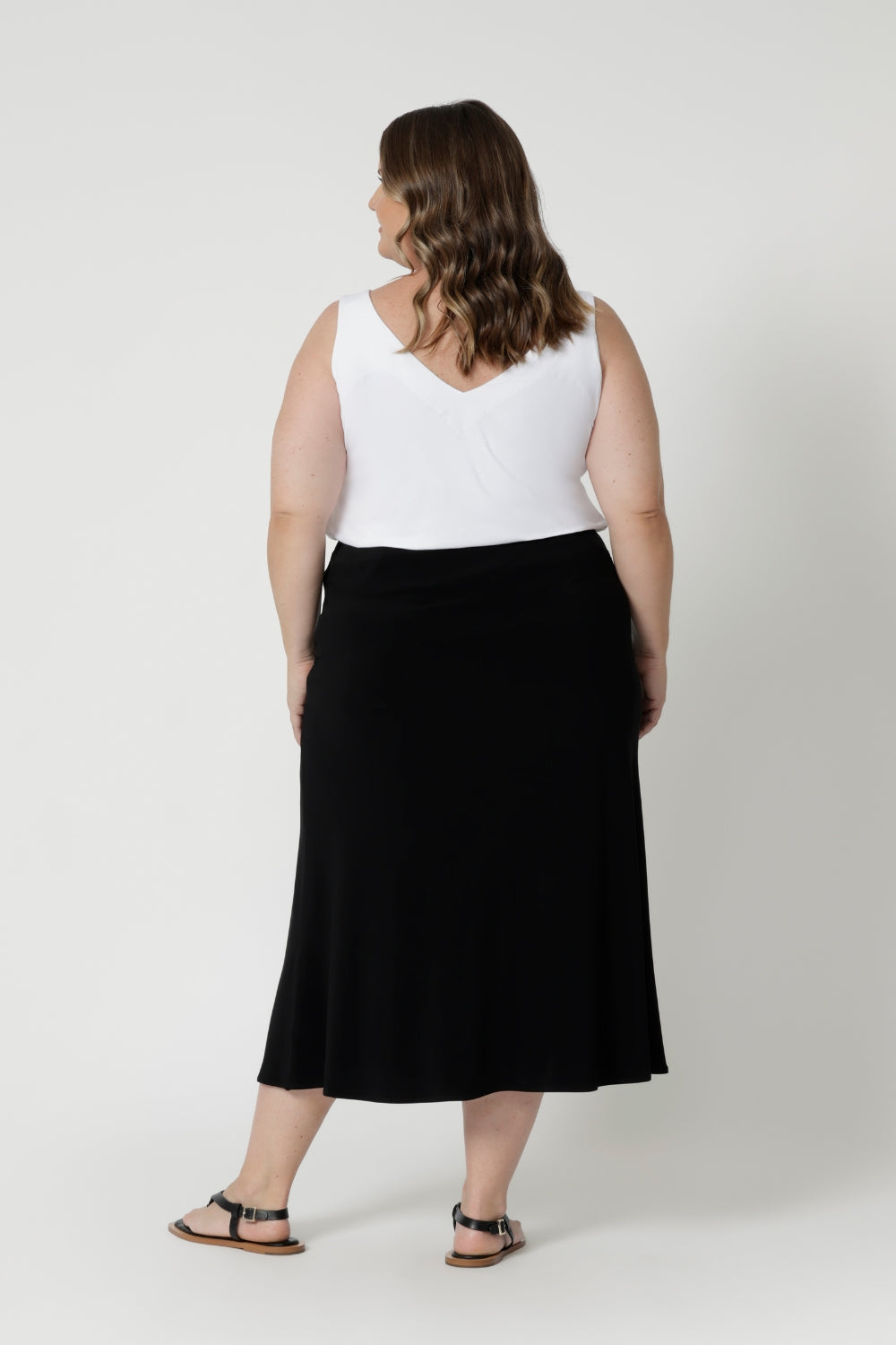 Plus sized woman wears black midi skirt paired with vanilla coloured cami and a black sandal for an easy day look perfect for travel or a day full of errands. Fashion brand Leina & Fleur have considered various body shapes and sizes when designing this skirt, ensuring it is comfortable and provides carefree movement for all. Asher skirt in black available in sizes 8-24.