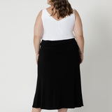 Plus sized woman wears black midi skirt paired with vanilla coloured cami and a black sandal for an easy day look perfect for travel or a day full of errands. Fashion brand Leina & Fleur have considered various body shapes and sizes when designing this skirt, ensuring it is comfortable and provides carefree movement for all. Asher skirt in black available in sizes 8-24.