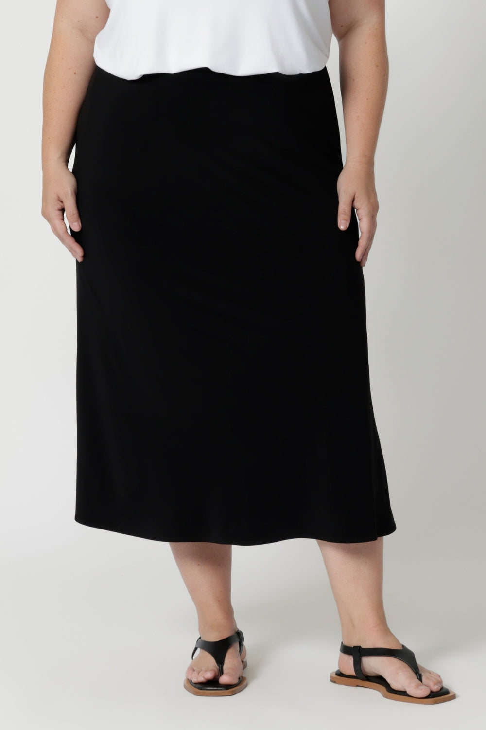 Made from soft-touch black jersey fabric, it feels luxuriously smooth against the skin while offering all-day breathability and ease. The bias-cut design creates natural shaping, gently skimming your curves for a flattering, feminine silhouette without being restrictive. Worn on size 18 woman on the go, styling her midi skirt with white t-shirt & sandals. 