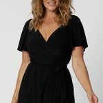 A size 10 midsize woman over 40 is wearing a maxi wrap dress in black. Made in Australia by Australian fashion brand Leina & Fleur in sizes 8 to 24.