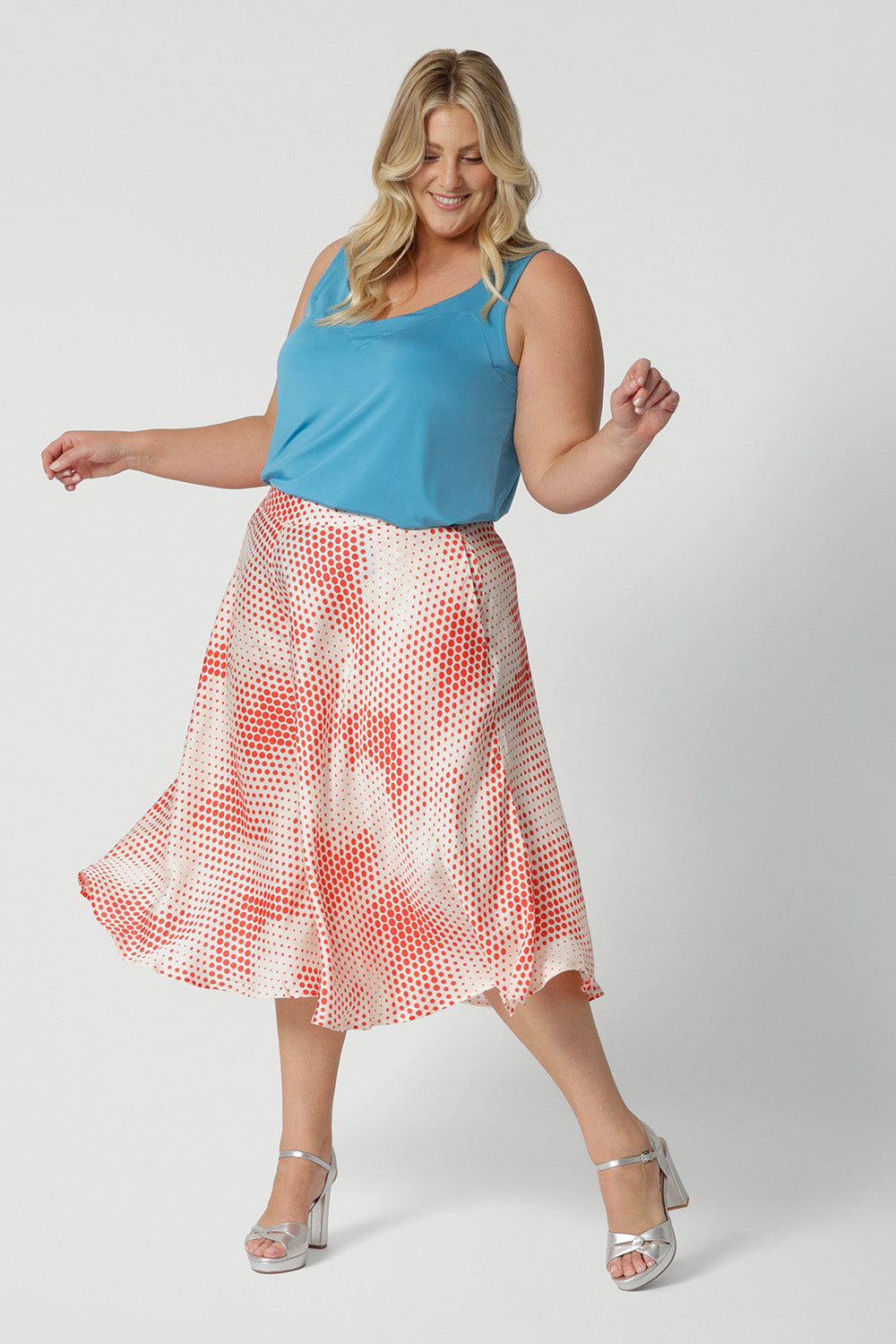 A good wedding guest outfit for plus size women,  a curvy, size 18 woman wears orange-red polka dot print culottes in luxurious Italian viscose fabric. Made in Australia by women's clothing brand, Leina & Fleur, these curve culottes are worn with a plus size cami top in mineral blue. Shop this summer wedding guest and event wear outfit online in sizes 8 to 24.