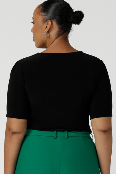 Back view of a curvy woman wearing a plus size, short sleeve black top with square neckline. A slim fit top in classic black, this tailored jersey top wears well with workwear separates for an office look and also as a smart casual top. Shop tops in petite, mid size and plus size online at Australian women's clothing brand, Leina & Fleur.
