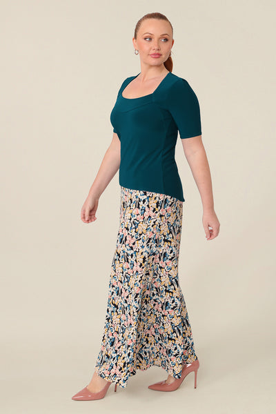 A size 12 curvy woman wears the short sleeve Berni Top in dark teal stretch jersey. The top has a squared scoop neckline, a structured bust and short sleeves. The top is paired with full-length wide leg printed pants for a casual look. Made in Australia, buy women's jersey tops in sizes 8 to size 24 online at Leina and Fleur.