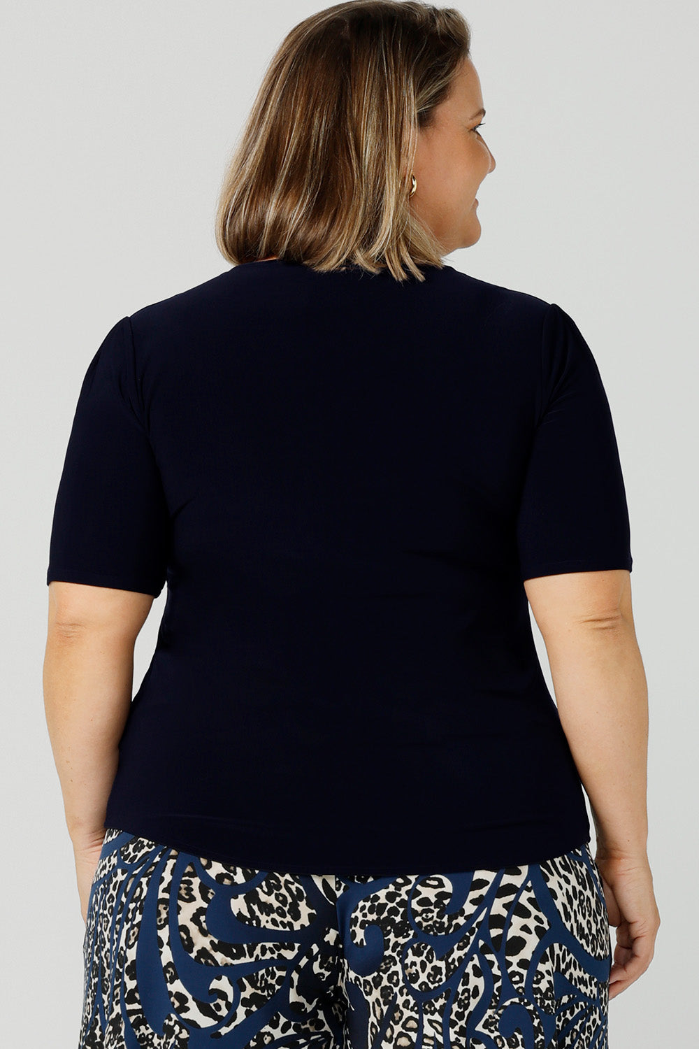 Back view of A petite height size, size 16 woman wears a casual jersey top in navy blue. This Australian-made women's top has short fitted sleeves, a square neckline and and high-low - perfect for weekend casual and travel capsule wardrobes.