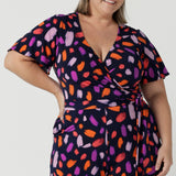 Close up of a size 18 curvy woman wears the Blanca Jumpsuit in Palette. A wrap jumpsuit design with a flutter sleeve, navy base colour and vibrant fuchsia, red, purple brush strokes throughout the print. Cropped leg length and petite to plus size friendly. Made in Australia for women size 8 - 24.
