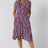 Summer dresses for over 40s women don't get much beter than this! A size 12, over 40 woman wears knee length summer dress with asymmetric hemlineand cowl neck. A short sleeve dress in pretty red, pink, white and navy print this is a good jersey dress for travel and cruise wear.  Made in Australia by Australian and New Zealand women's clothes brand, Leina & Fleur, shop their petite to plus size dresses online. 