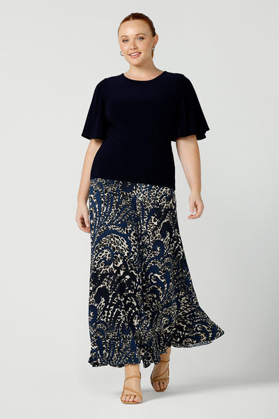 A curvy size 12 woman wears a jersey top in navy blue, styled with animal print, wide leg pants. This Australian-made women's top has flutter sleeves, a high, round neckline and and high-low hem perfect for weekend casual and travel capsule wardrobes.