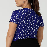 Back view of a size 12 woman wearing a cobalt blue spot top with flutter sleeves, high low hemline and v-neck. Soft slinky jersey. Made in Australia for women size 8 to 24.