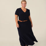 A petite woman with curve wears a navy blue V-neck top with short sleeves with a navy blue maxi skirt and tan belt. A good work top for plus size women, this tailored top is made in Australia by Australian fashion brand, Leina & Fleur in sizes 8 to 24.