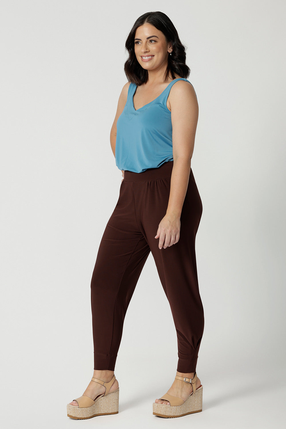 Side view of good travel pants for petite women. Worn with a mineral blue cami top with wide shoulder straps, these tapered leg pants by Australian and New Zealand women's clothes brand, Leina & Fleur are a comfortable stretchy pant in espresso brown jersey fabric. Shop pants for petite height women online in sizes 8 to 24.