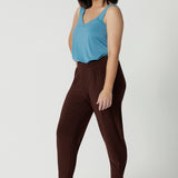 Side view of good travel pants for petite women. Worn with a mineral blue cami top with wide shoulder straps, these tapered leg pants by Australian and New Zealand women's clothes brand, Leina & Fleur are a comfortable stretchy pant in espresso brown jersey fabric. Shop pants for petite height women online in sizes 8 to 24.