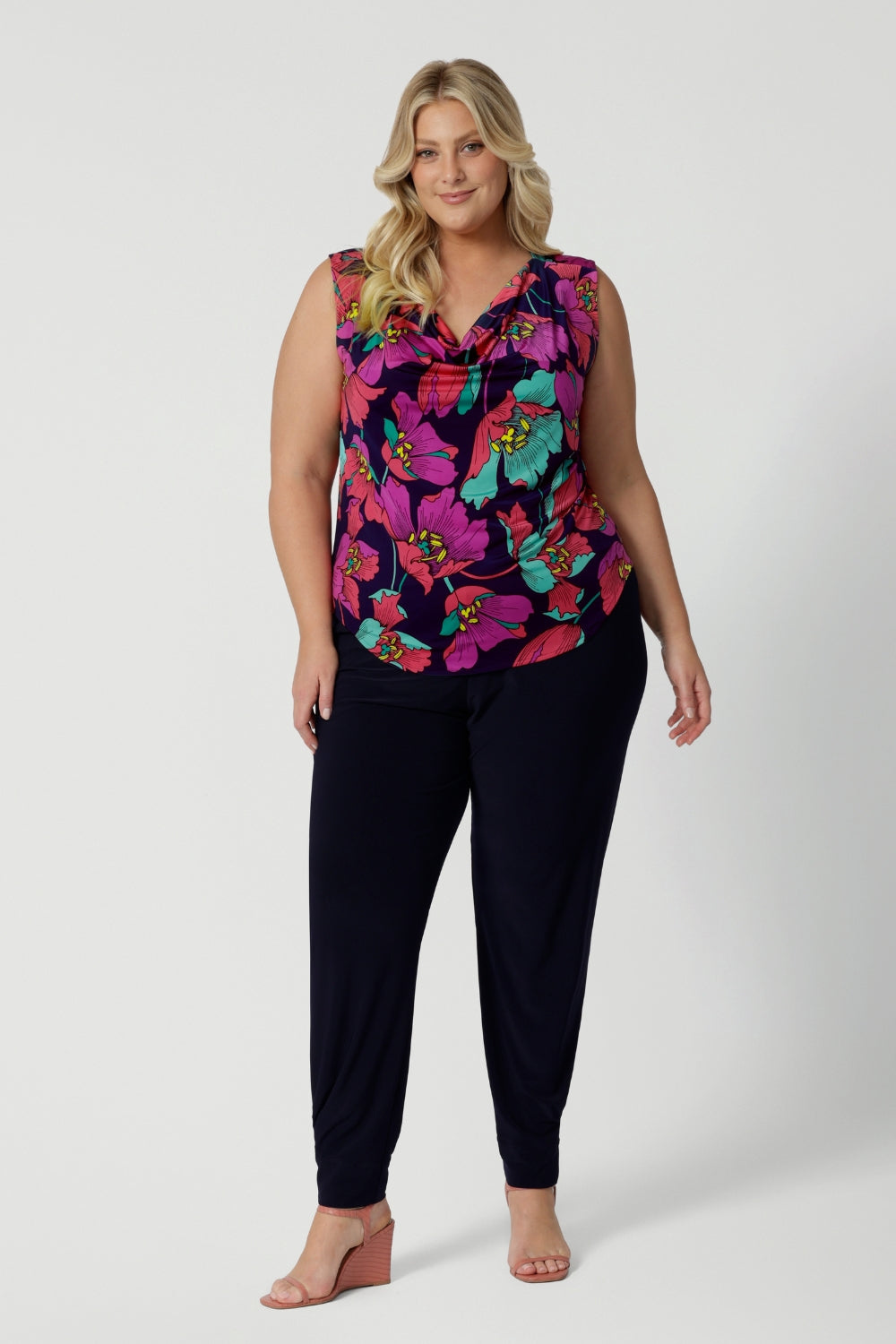 An image of a summer top for curvy women, a size 18, plus size women wears a cowl neck jersey top. This sleeveless top has a bold floral print - great for corporate wear as well as casual wear. Styled with a navy travel pant. Made in Australia by Australian and New Zealand clothing brand, Leina & Fleur, shop this top in petite to plus sizes. 