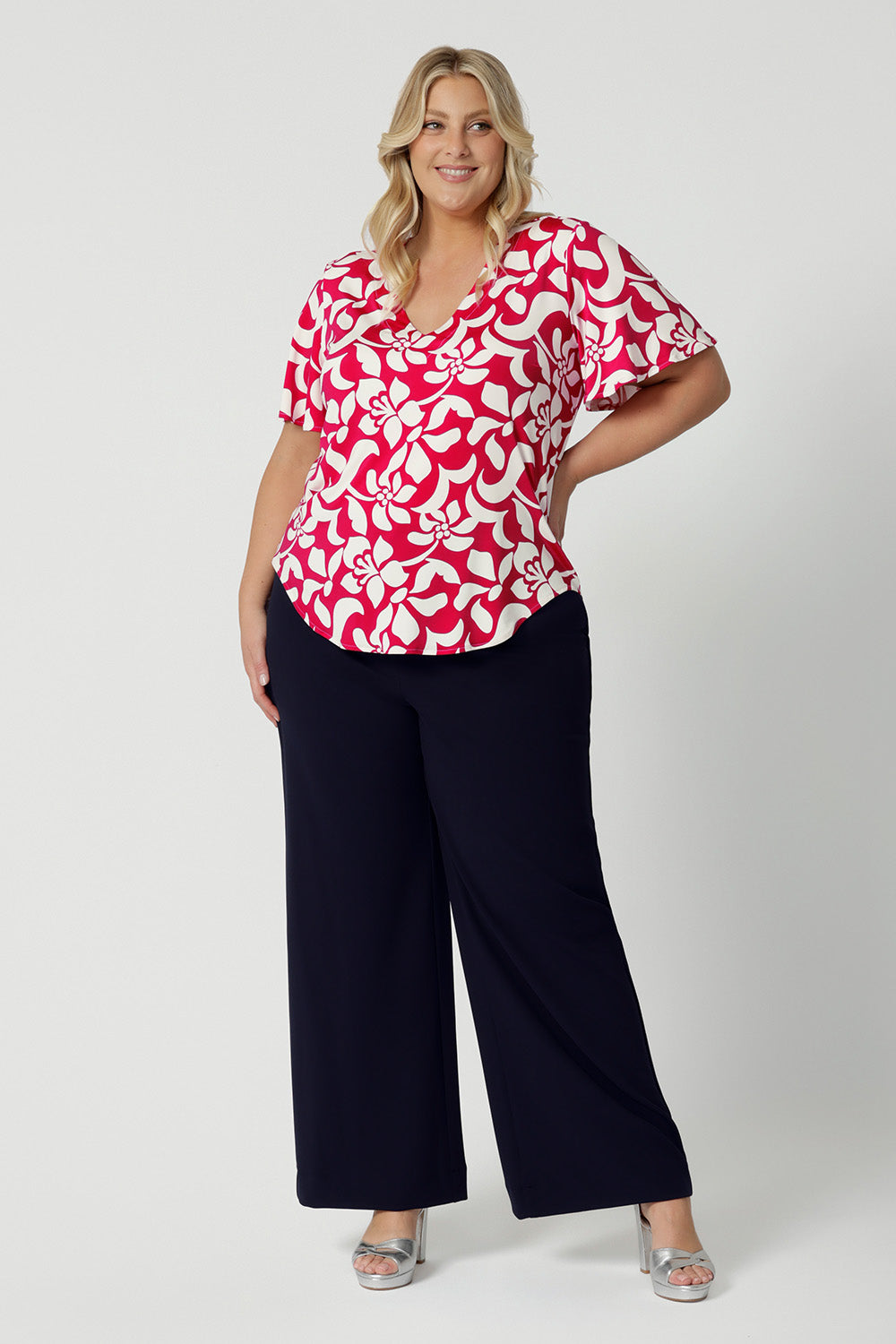 Plus sized woman wear summer ready top that is the perfect blend of comfort and style, with a delicate flutter sleeves that adds a touch of femininity and movement. The top comes in a sophisticated red base with a striking ivory floral design. Made from dry-touch jersey, this fabric offers a breathable soft feel, ideal for summer months. To ensure you stay cool and comfortable throughout the day.  Leina & Fleur stock sizes 8-24.