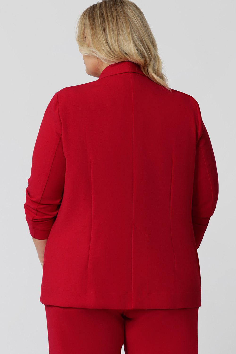 Back view of a size 18 woman wearing the Merit Blazer in Flame, a textured scuba crepe plus size blazer with button front. This red work blazer is worn with red workwear pants and navy work top. Curved hemline and front pockets. This blazer is Made in Australia for curvy women size 8 - 24.