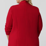 Back view of a size 18 woman wearing the Merit Blazer in Flame, a textured scuba crepe plus size blazer with button front. This red work blazer is worn with red workwear pants and navy work top. Curved hemline and front pockets. This blazer is Made in Australia for curvy women size 8 - 24.