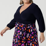 Close up of a size 18 curvy woman wears the Nerida dress. Functioning fit and flare wrap dress with a navy bodice and printed skirt. 3/4 Sleeves and functioning pockets. Made in Australia for women. Size 8 - 24. Styled back with a brown sling back heel.