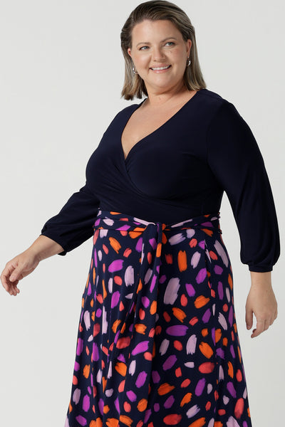 Close up of a size 18 curvy woman wears the Nerida dress. Functioning fit and flare wrap dress with a navy bodice and printed skirt. 3/4 Sleeves and functioning pockets. Made in Australia for women. Size 8 - 24. Styled back with a brown sling back heel.
