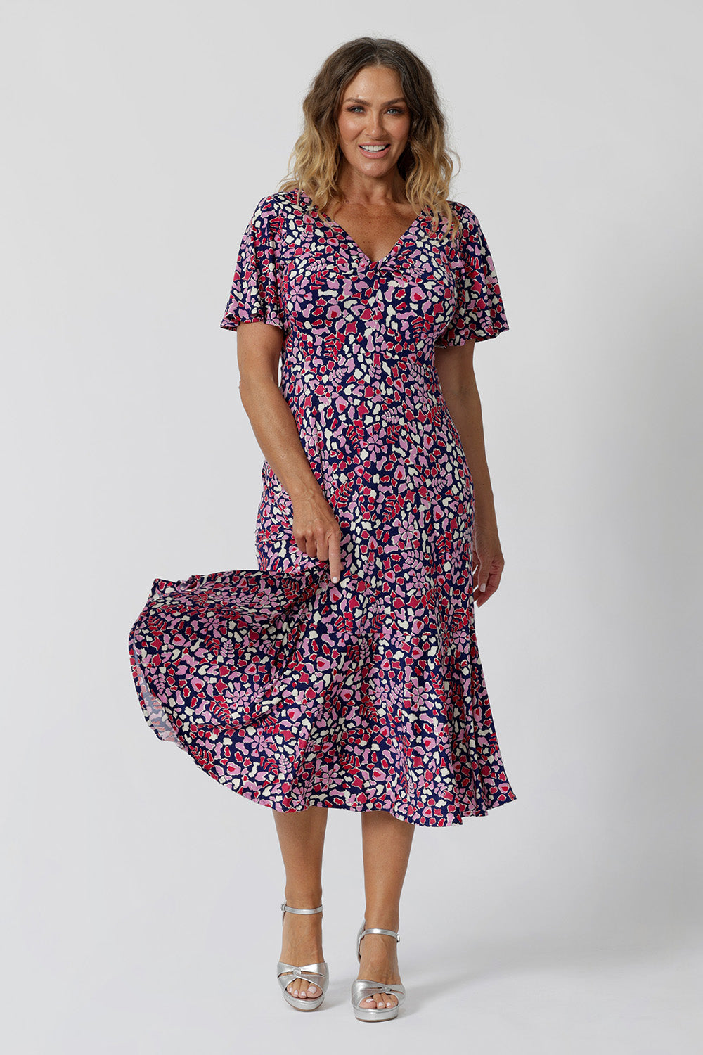 Summer dresses for over 50s women doen't get much beter than this! A size 12, over 50 woman wears an empire line midi dress with flutter sleeves and twist front bodice. A good dress for cruise wear, the pink, red, white and navy blue print make it a pretty summer dress. Made in Australia by Australian and New Zealand women's clotheing label, Leina & Fleur, shop their petite to plus size dresses online. 