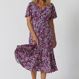 Summer dresses for over 50s women doen't get much beter than this! A size 12, over 50 woman wears an empire line midi dress with flutter sleeves and twist front bodice. A good dress for cruise wear, the pink, red, white and navy blue print make it a pretty summer dress. Made in Australia by Australian and New Zealand women's clotheing label, Leina & Fleur, shop their petite to plus size dresses online. 