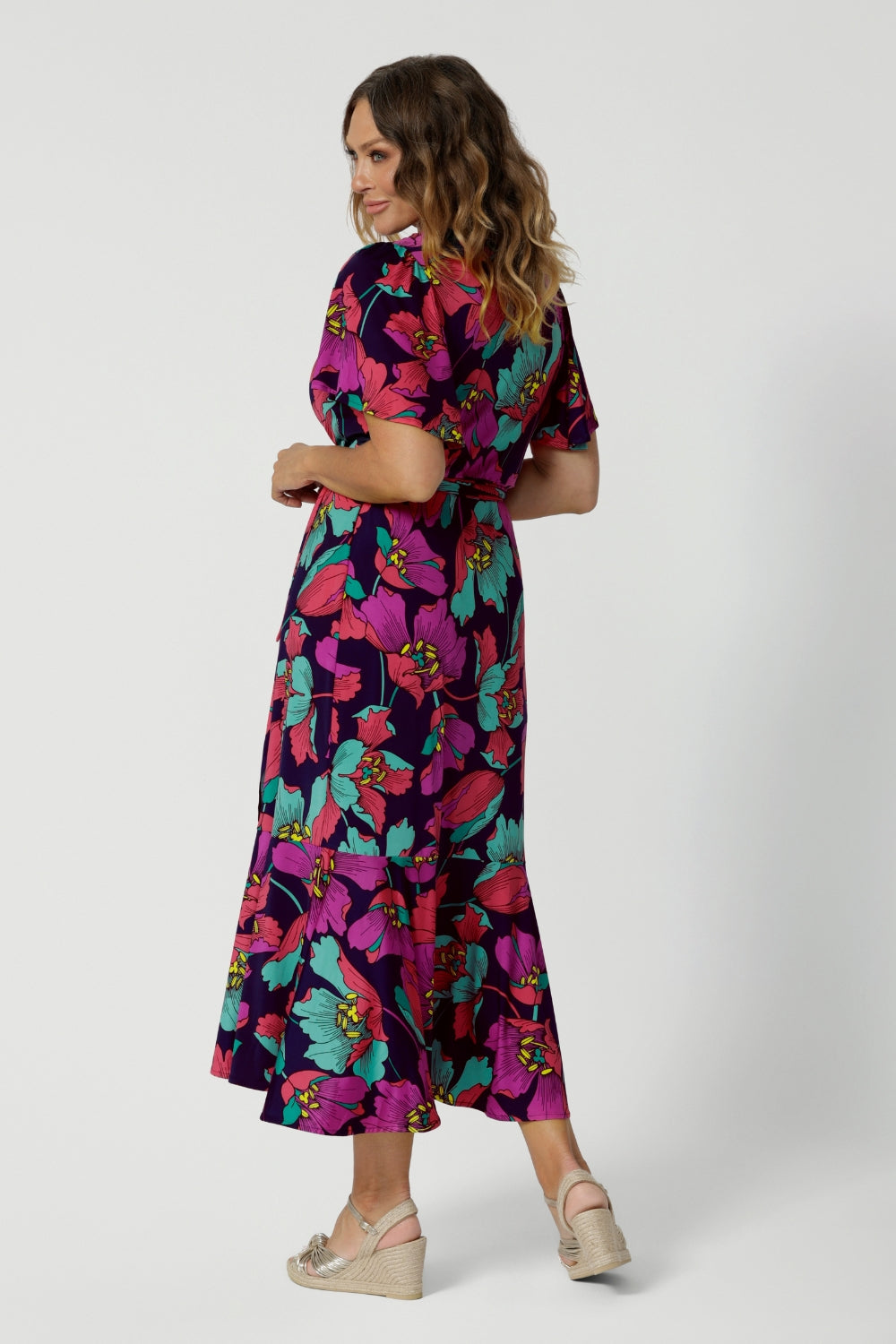 A photo if the back of A size 10 woman over 40 wears a maxi wrap dress in a bold print. An elegant wrap dress with a tiered ruffle skirt,  sweetheart neckline and flutter sleeve. Made in Australia for women size 8 - 24 by Leina & Fleur.