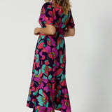 A photo if the back of A size 10 woman over 40 wears a maxi wrap dress in a bold print. An elegant wrap dress with a tiered ruffle skirt,  sweetheart neckline and flutter sleeve. Made in Australia for women size 8 - 24 by Leina & Fleur.