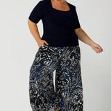 A petite height size, size 16 woman wears a casual jersey top in navy blue, styled with animal print, wide leg pants. This Australian-made women's top has short fitted sleeves, a square neckline and and high-low - perfect for weekend casual and travel capsule wardrobes.