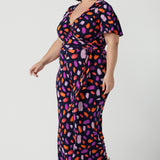 Size 18 curvy woman wears the Blanca Jumpsuit in Palette. A wrap jumpsuit design with a flutter sleeve, navy base colour and vibrant fuchsia, red, purple brush strokes throughout the print. Cropped leg length and petite to plus size friendly. Made in Australia for women size 8 - 24.