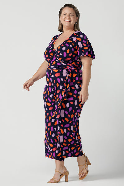 Size 18 curvy woman wears the Blanca Jumpsuit in Palette. A wrap jumpsuit design with a flutter sleeve, navy base colour and vibrant fuchsia, red, purple brush strokes throughout the print. Cropped leg length and petite to plus size friendly. Made in Australia for women size 8 - 24.