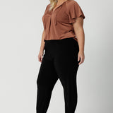 A good summer top for over plus size women, a size 18 woman wears a flutter sleeve top in clay slinky jersey fabric. An easy-care top for travel and cruise wear, this made-in-Australia V neck top is worn with tapered leg black travel pants.  By Australian and New Zealand women's clothes label, Leina and Fleur shop petite to plus size tops for women  online.