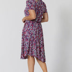 Back view of a summer dress for over 40s women. A size 12, over 40 woman wears knee length summer dress with asymmetric hemlineand cowl neck. A short sleeve dress in pretty red, pink, white and navy print this is a good jersey dress for travel and cruise wear.  Made in Australia by Australian and New Zealand women's clothes brand, Leina & Fleur, shop their petite to plus size dresses online. 
