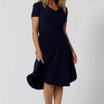 Navy dresses for over 40s women don't get much beter than this! A size 12, over 40 woman wears knee length summer dress with asymmetric hemlineand cowl neck. A short sleeve dress in navy jersey fabric, this is an easy-care dress and makes a good jersey dress for travel and cruise wear.  Made in Australia by Australian and New Zealand women's clothes brand, Leina & Fleur, shop their petite to plus size dresses online. 