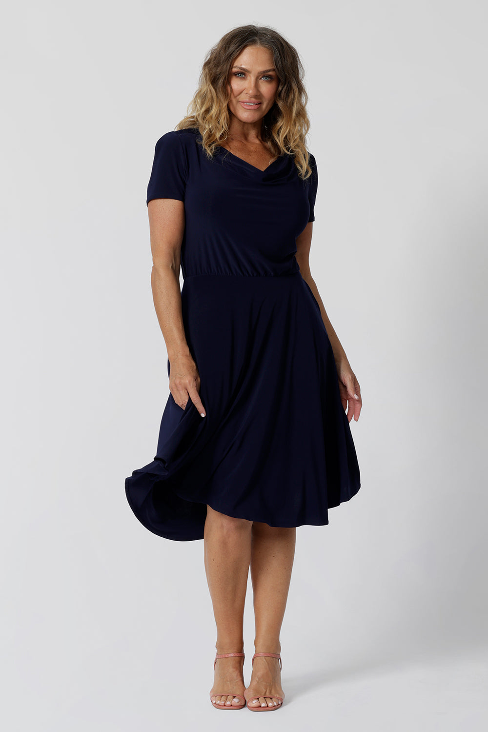 Navy dresses for over 40s women don't get much beter than this! A size 12, over 40 woman wears knee length summer dress with asymmetric hemlineand cowl neck. A short sleeve dress in navy jersey fabric, this is an easy-care dress and makes a good jersey dress for travel and cruise wear.  Made in Australia by Australian and New Zealand women's clothes brand, Leina & Fleur, shop their petite to plus size dresses online. 