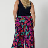 An image of the back of a curvy size 18 woman wearing the Caspian Palazzo pant in a bright floral print. In soft and lightweight jersey this pant features side pockets and a flared leg opening. Made in sizes 8 to 24 by Australian fashion brand Leina & Fleur.