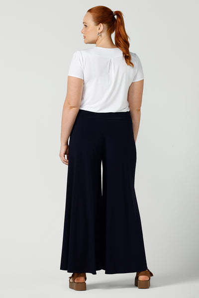 Back view of a curvy size, size 12 woman wears wide leg pants with pockets with a white bamboo top. These pull-on, easy care pants are comfortable for your everyday workwear capsule wardrobe. Shop these Australian-made wide leg trousers online in sizes 8 to 24, petite to plus sizes.