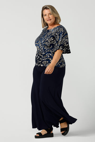 A petite height size 16 woman wears a jersey top in animal print, styled with navy wide leg pants. This Australian-made women's top has flutter sleeves, a high, round neckline and and high-low hem perfect for weekend casual and travel capsule wardrobes.