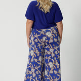 Wide leg pants for summer don't come much better than this! Worn by a size 18, curvy woman, this is a back view of plus size wide leg pants are in easy care jersey with a blue, caramel and white floral print. Made in Australia by Australian and New Zealand women's clothes brand, Leina and Fleur. Shop wide leg pants in petite to plus sizes.