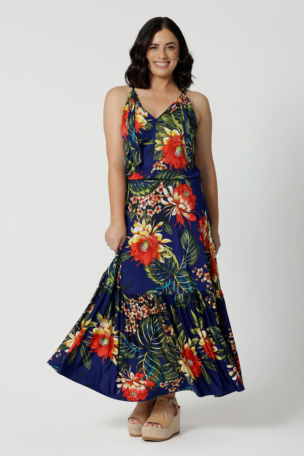 Full body image of a petite woman wears floral printed maxi dress. This travel ready dress has a halter neck and a ruffle skirting. Easy care fabric has a floral design with orange and yellow flowers on a navy base. This Australian made dress is comfortable and gives great stretch. Leina and Fleur is a women’s clothing company that actively stocks plus sizes & petite sizes ranging from 8 to 24.