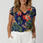 40 year old woman wears floral top with a cowl neck detail. This easy care top is made from easy care slinky jersey fabric. Floral printed design has a colourful combination of orange, yellow and white flowers on a deep blue base. This top is perfect for any travel capsule. Designed in Australia for Australian and New Zealand women. Leina & Fleur is a woman's clothing brand that stock sizes from 8 to 24. Shop this summer ready dress in petite sizes and plus sizes.