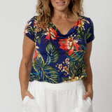 40 year old woman wears floral top with a cowl neck detail. This easy care top is made from easy care slinky jersey fabric. Floral printed design has a colourful combination of orange, yellow and white flowers on a deep blue base. This top is perfect for any travel capsule. Designed in Australia for Australian and New Zealand women. Leina & Fleur is a woman's clothing brand that stock sizes from 8 to 24. Shop this summer ready dress in petite sizes and plus sizes.