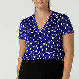 Size 12 Woman wears a cobalt blue spot top with flutter sleeves, high low hemline and v-neck. Soft slinky jersey. Made in Australia for women size 8 to 24.