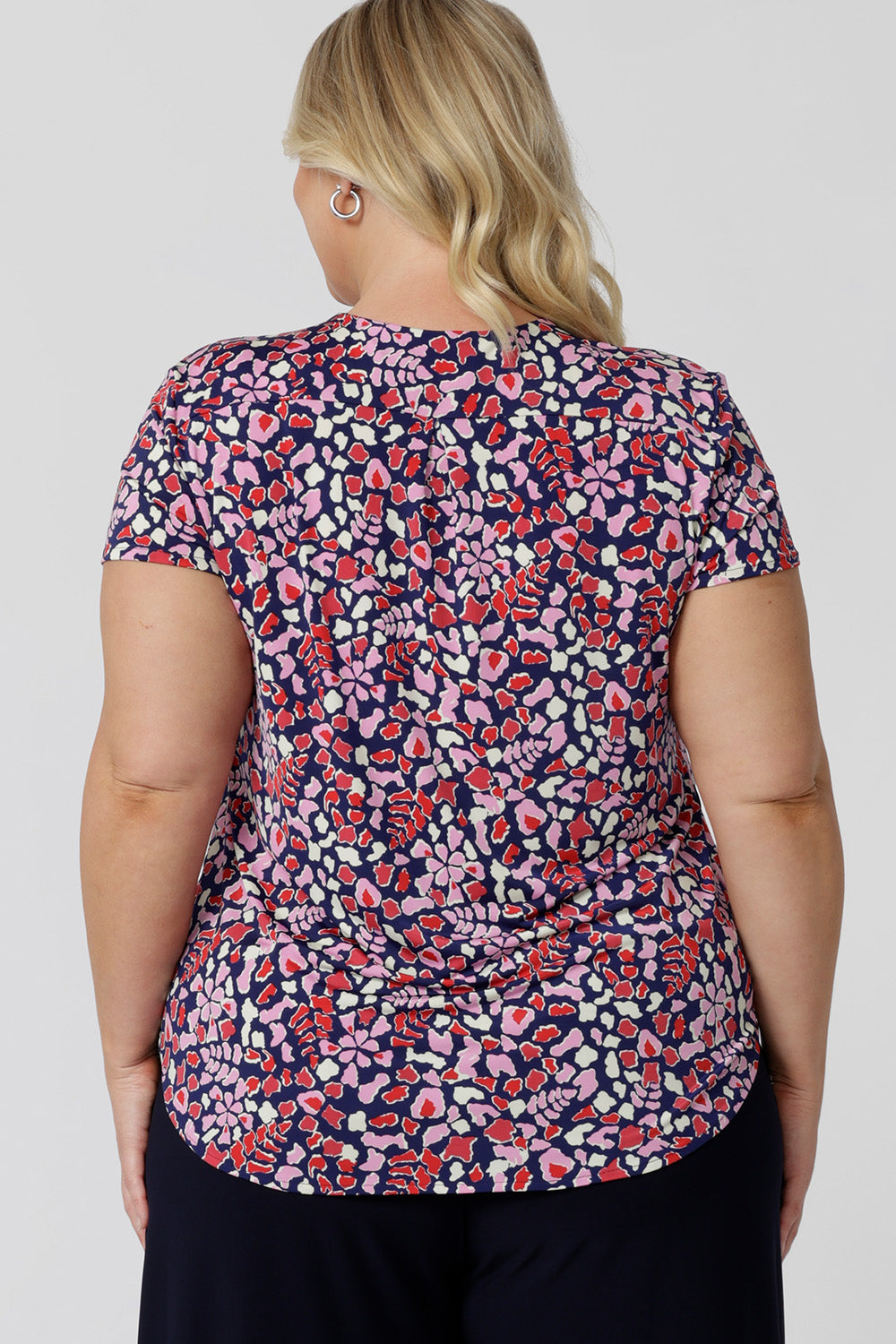 Back viewof a work  top for plus size women. This V-neck top with tailroed tuck is a comfortable top for women.  A size 18 woman wears a a plus size short sleeve V-neck jersey top in red, pink, white and navy print. Made in Australia top by Australian and New Zealand women's clothes brand, Leina & Fleur, shop their petite to plus size tops online. 