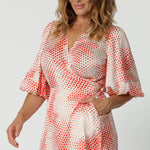 Close up view of the bodice of a good dress for over 40s women, this silky wrap dress has an orange spot print and 3/4 lantern-shaped sleeves. Made in Australia by women's clothing brand, Leina & Fleur, wear this 3/4 sleeve wrap dress for wedding guest outfit and summer event  wear. Shop this summer wedding guest and event wear outfit online in sizes 8 to 24.
