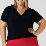  A curvy size 18 woman wears a navy jersey top great for corporate wear.  Styled back with a fuchsia pink tube skirt. This tailored top with short sleeves and a v-neckline is made in Australia by Australian fashion brand, Leina & Fleur in sizes 8 to 24.