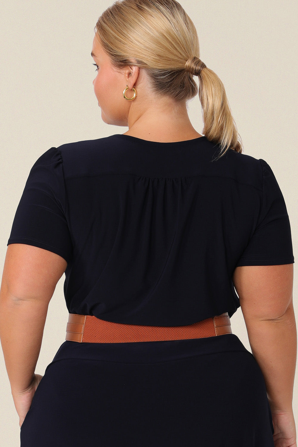 Back view of a petite woman with curve wears a navy blue V-neck top with short sleeves. A good work top for plus size women, this tailored top is made in Australia by Australian fashion brand, Leina & Fleur in sizes 8 to 24.