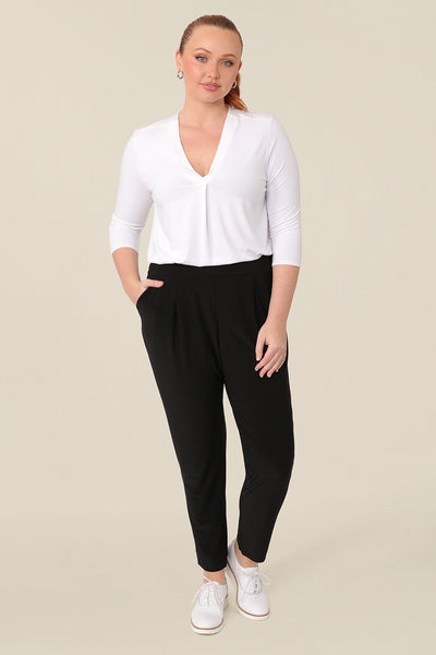 A great top for curvy women, this white bamboo jersey top is tailored with a pleat below the V-neck. Lightweight and breathable, this 3/4 sleeve top makes a comfortable work top, looking classic under workwear jackets and suits. A classic top worn with dropped crotch, cropped black travel pants, this white jersey top is good for casual wear and travel capsule wardrobes too. Shown on a curvy, mid size woman, this top is also available in petite and plus sizes online at women's clothing brand, Leina & Fleur. 