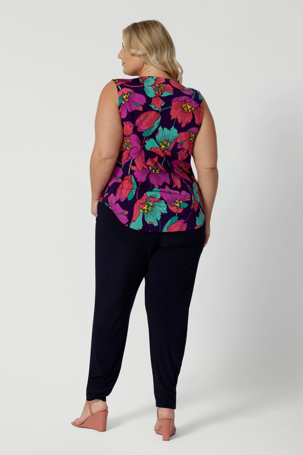 An image of the back of a summer top for curvy women, a size 18, plus size women wears a cowl neck jersey top. This sleeveless top has a bold floral print - great for corporate wear as well as casual wear. Styled with a navy travel pant. Made in Australia by Australian and New Zealand clothing brand, Leina & Fleur, shop this top in petite to plus sizes. 