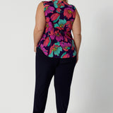 An image of the back of a summer top for curvy women, a size 18, plus size women wears a cowl neck jersey top. This sleeveless top has a bold floral print - great for corporate wear as well as casual wear. Styled with a navy travel pant. Made in Australia by Australian and New Zealand clothing brand, Leina & Fleur, shop this top in petite to plus sizes. 